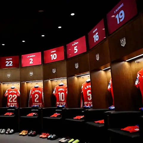 Un vestiaire avec des maillots rayés rouge et blanc sous des cabines éclairées, et un logo au plafond.