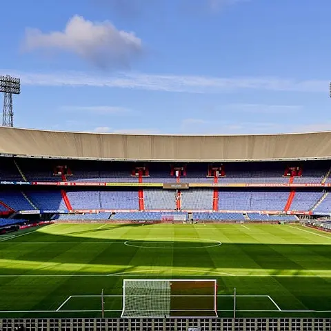 Un garçon portant un maillot vert et blanc pose pour une photo dans un stade, avec une personne capturant le moment sur un téléphone.
