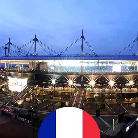Un grand stade vide, avec des sièges en gradins et des lumières vives, montrant un terrain vert et un ciel clair au-dessus.