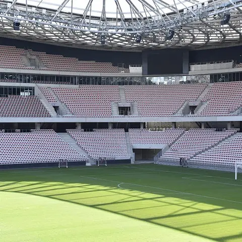 Stade vide avec des sièges en gradins et un toit en treillis, donnant sur un terrain en herbe bien entretenu. Aucune personne n'est présente.