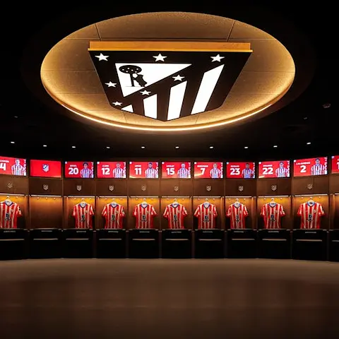 A locker room with arranged red and white striped jerseys under illuminated cubicles, and a logo on the ceiling.